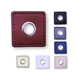 Könnte beinhalten: Sortiment quadratischer Lederösen in verschiedenen Farben, darunter Rot, Schwarz, Blau, Beige und Weiß. Jede Öse hat einen silbernen Metallring in der Mitte.