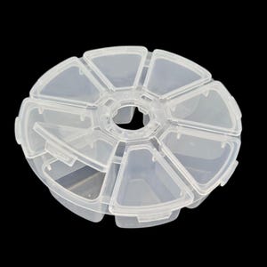 Può includere: Una scatola di contenimento rotonda in plastica trasparente con un coperchio girevole. La scatola ha otto scomparti, ognuno a forma di triangolo. Gli scomparti sono perfetti per riporre piccoli oggetti come perline, bottoni o gioielli.