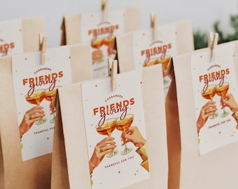 May include: Brown paper gift bags with tags that read "Friends Giving" and "Thankful for You." The tags feature illustrations of champagne glasses and hands clinking. Each bag is clipped with a small wooden clothespin.
