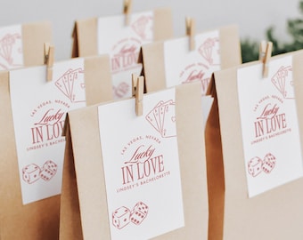 Può includere: Buste di carta marrone con etichette bianche che recitano "Las Vegas, Nevada Lucky in Love Lindsey's Bachelorette" con un dado rosso e una grafica di carte da gioco.
