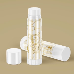 May include: White and gold lip balm tubes with a striped pattern and gold illustrations of glasses, hearts, and bees. One tube has the text "Found Her Honey March 2026". The cap is off one tube.