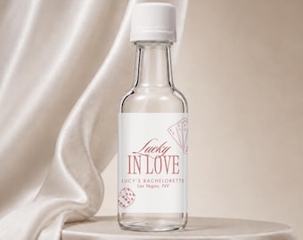 Può includere: Una bottiglia in vetro trasparente con tappo a vite bianco e un'etichetta con il testo Lucky IN LOVE, LUCY'S BACHELORETTE, Las Vegas, NV, accompagnata da illustrazioni di carte da gioco e un dado in rosso tenue su sfondo bianco.