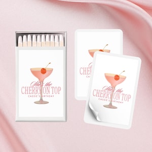 Könnte beinhalten: Ein Set weißer Streichholzschachteln mit einer rosa und weißen Illustration eines Cocktails mit einer Kirsche obenauf. Der Text auf der Streichholzschachtel lautet "She's the Cherry on Top Cassie's Birthday".