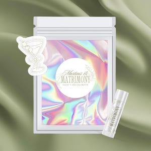 May include: A white zippered pouch with a holographic iridescent background. The pouch contains a white lip balm with the text "Martini's & Matrimony Haley's Bachelorette" and a sticker with a martini glass and the text "Haley's Bachelorette".