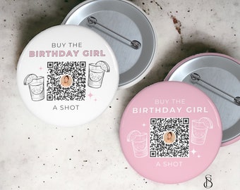 May include: Two round white and pink pinback buttons with the text "BUY THE BIRTHDAY GIRL A SHOT". Each button features a QR code and a cocktail illustration. The buttons have a silver pin on the back.