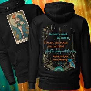 May include: Black hoodie featuring a tarot card design with a woman in a teal dress and the text "THE SHOWGIRL." The back of the hoodie has text that reads "You want a fight? You found it." and other phrases.