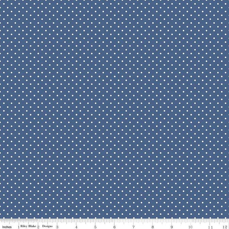 May include: A blue fabric featuring a repeating pattern of small white polka dots. A white ruler is visible along the bottom edge, showing a measurement scale from 0 to 12 inches, with the text Riley Blake Designs printed on it.