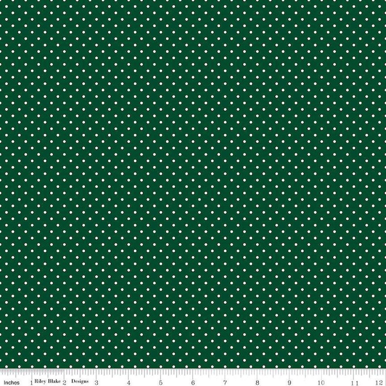 May include: A dark green fabric featuring a repeating pattern of small white polka dots. A white ruler is visible at the bottom edge, showing a scale of 12 inches, with the text Riley Blake Designs printed along the measurement line.