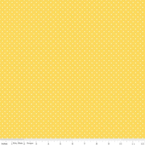 May include: A bright yellow fabric featuring a repeating pattern of small white polka dots. A white ruler is visible at the bottom edge, showing measurements in inches from 0 to 12, with the text Riley Blake Designs printed on it.