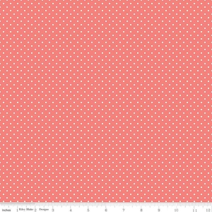 May include: A coral pink fabric featuring a repeating pattern of small white polka dots. A white ruler is visible along the bottom edge, showing a scale of 12 inches, with the text Riley Blake Designs printed near the left side.