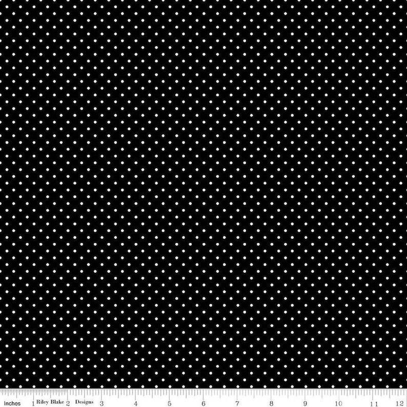 May include: A black fabric featuring a repeating pattern of small white polka dots, displayed alongside a white ruler measuring 12 inches to provide a clear scale of the textile design and the size of the dots.