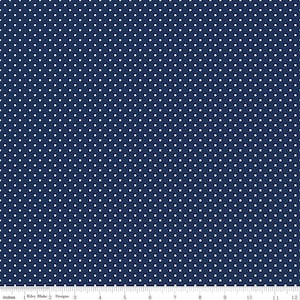 May include: A navy blue fabric featuring a repeating pattern of small white polka dots. A white ruler is visible at the bottom edge, showing a scale of 12 inches, with the text Riley Blake Designs printed along the measurement markings.