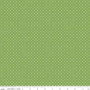 May include: A green fabric featuring a repeating pattern of small white polka dots. A ruler is visible at the bottom edge, showing a scale of 12 inches, with the text Riley Blake Designs printed along the measurement markings.