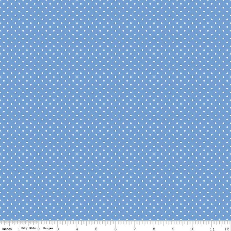 May include: A light blue fabric featuring a repeating pattern of small white polka dots. A white ruler is visible at the bottom edge, showing a scale of 12 inches, with the text Riley Blake Designs printed along the measurement line.