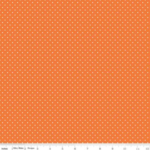 May include: A vibrant orange fabric featuring a repeating pattern of small white polka dots. A white ruler is visible at the bottom edge, showing a scale of 12 inches, with the text Riley Blake Designs printed near the left side.