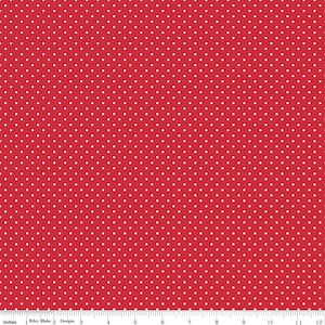 May include: A red fabric featuring a repeating pattern of small white polka dots. A white ruler is visible at the bottom edge, showing a scale of 12 inches, with the text Riley Blake Designs printed along the measurement markings.