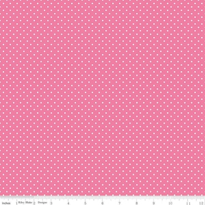 May include: A pink fabric featuring a repeating pattern of small white polka dots. At the bottom, a white ruler shows measurements in inches, with the text Riley Blake Designs printed clearly along the edge of the fabric.