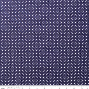 May include: A dark purple fabric featuring a repeating pattern of small white polka dots. A white ruler is visible at the bottom edge, showing a scale of 12 inches, with the text Riley Blake Designs printed near the left side.