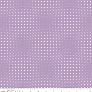 May include: A light purple fabric featuring a repeating pattern of small white polka dots. A ruler at the bottom edge shows a scale of 12 inches, with the text Riley Blake Designs printed near the one-inch mark.