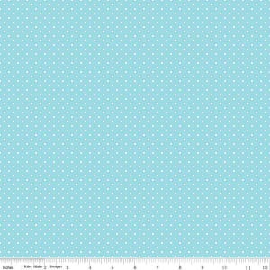 May include: A light blue fabric featuring a repeating pattern of small white polka dots. A white ruler is visible at the bottom edge, showing measurements in inches from 0 to 12, with the text Riley Blake Designs printed near the start.
