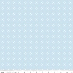 May include: A light blue fabric featuring a repeating pattern of small white polka dots. A ruler at the bottom edge shows a scale of 12 inches, with the text Riley Blake Designs printed near the left side of the measurement scale.