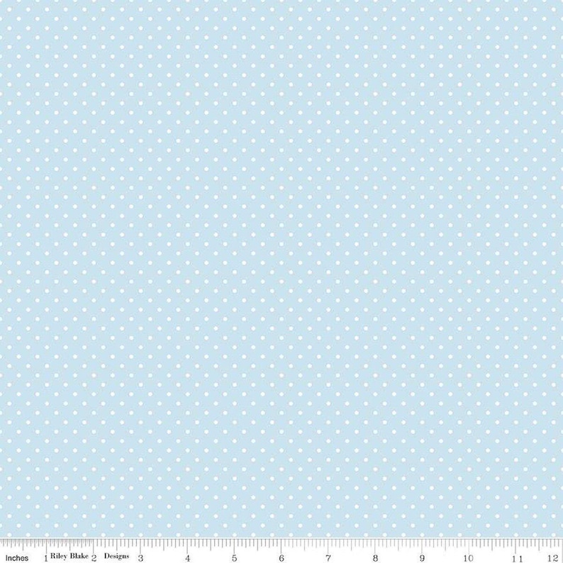May include: A light blue fabric featuring a repeating pattern of small white polka dots. A ruler at the bottom edge shows a scale of 12 inches, with the text Riley Blake Designs printed near the left side of the measurement scale.