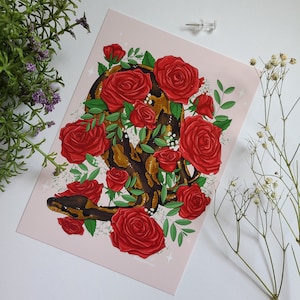 Może przedstawiać: Czerwono-brązowy wąż owinięty wokół bukietu czerwonych róż. Wąż jest zwinięty, a róże są ułożone wokół niego. Tło jest jasnoróżowe.