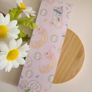 Puede incluir: Un marcapáginas de patrón rosa y blanco con ilustraciones de geckos que llevan sombreros de fiesta y sostienen globos. Los geckos están en varias poses, algunos están de pie, algunos están sentados y algunos están saltando. El fondo es rosa claro con lunares blancos.