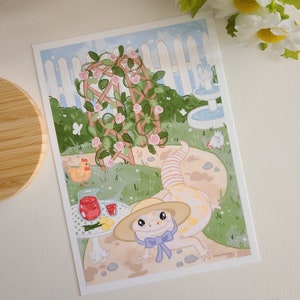 Może przedstawiać: Biało-żółta jaszczurka w słomkowym kapeluszu z niebieską wstążką siedzi na ścieżce w ogrodzie. Ogród ma białe drewniane ogrodzenie, pergolę z różami, fontannę i małego kurczaka.