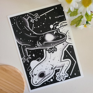 Może przedstawiać: Czarno-biała ilustracja dwóch gekonów na tle nocnego, gwieździstego nieba. Jeden gekon patrzy w lewo, a drugi w prawo. Gecony są ze sobą splecione i wyglądają, jakby tańczyły. Tekst "@angel.dreams" znajduje się w prawym górnym rogu obrazu.