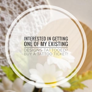 Może przedstawiać: Białe koło z czarnym obramowaniem i tekstem "INTERESTED IN GETTING ONE OF MY EXISTING DESIGNS TATTOOED? BUY A TATTOO TICKET!" Koło znajduje się przed rozmytym tłem z białymi kwiatami i zielonymi liśćmi.