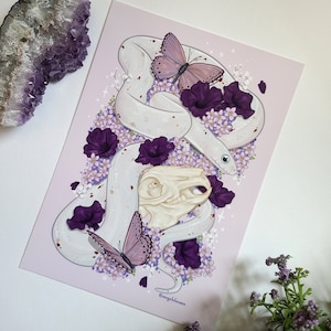 Puede incluir: Una serpiente blanca con flores moradas y una calavera en el centro. La serpiente está enroscada alrededor de la calavera y las flores florecen a su alrededor. El fondo es de color morado claro.