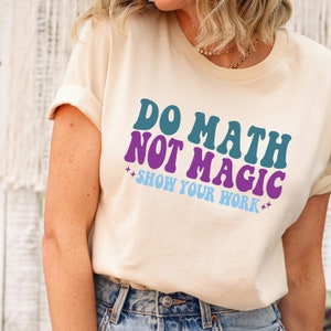 May include: A white t-shirt with the text "Do Math Not Magic Show Your Work" in a retro font. The text is in shades of teal, purple, and blue.
