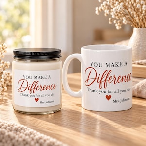 May include: A white ceramic mug and a glass candle jar with a black lid. Both items feature a white label with the text "YOU MAKE A Difference Thank you for all you do" in black and orange script, a small red heart, and the name "Mrs. Johnson".