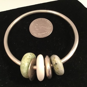 May include: A silver bangle bracelet with four beads. Two of the beads are green and white, and the other two are white.