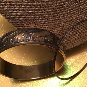 May include: Two black metal bangles. One bangle has a gold-toned design of fish and leaves. The other bangle has a simple, ornate design.