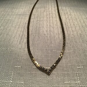 May include: A gold chain necklace with a V-shaped design of small clear stones.