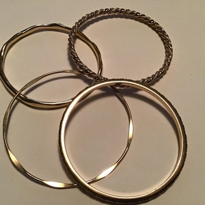 May include: Four gold-toned bangles, one with a braided design, one with a smooth finish, and two with a slightly textured finish.