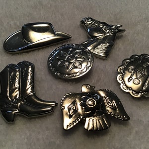 May include: A collection of silver-toned metal Western-themed embellishments. The set includes a cowboy hat, a horse head, a pair of cowboy boots, and several decorative round pieces with floral and geometric designs. These pieces are likely used for crafting or jewelry making.
