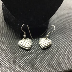 Puede incluir: Un par de pendientes de coraz&oacute;n colgantes de plata con una superficie texturizada.