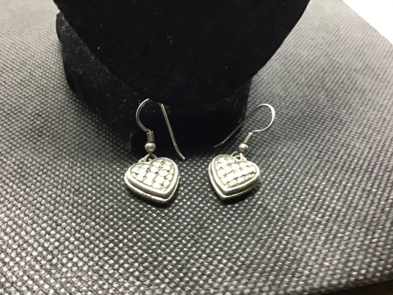 Puede incluir: Un par de pendientes de coraz&oacute;n colgantes de plata con una superficie texturizada.