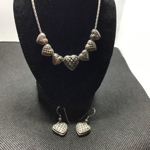 Puede incluir: Un collar y pendientes de plata con una cadena y colgantes en forma de coraz&oacute;n. Los corazones tienen un dise&ntilde;o texturizado y acolchado.