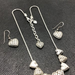 Puede incluir: Un collar de plata con un colgante de coraz&oacute;n y pendientes a juego. El collar tiene una cadena con m&uacute;ltiples colgantes de coraz&oacute;n. Los pendientes son simples y tienen un solo colgante de coraz&oacute;n.