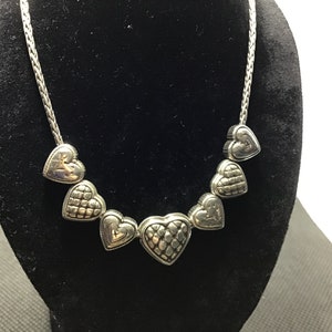 Puede incluir: Un collar de plata con una cadena y dijes en forma de coraz&oacute;n. Los corazones son texturizados y tienen un dise&ntilde;o ligeramente elevado.