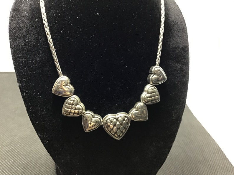 Puede incluir: Un collar de plata con una cadena y dijes en forma de coraz&oacute;n. Los corazones son texturizados y tienen un dise&ntilde;o ligeramente elevado.