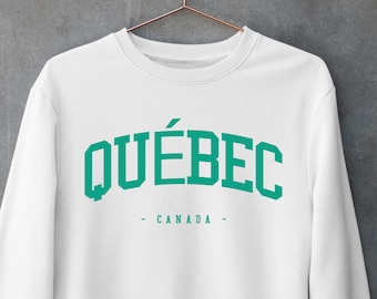 Puede incluir: Una sudadera blanca de manga larga con cuello redondo que presenta la palabra QUÉBEC en una fuente universitaria grande, arqueada y de color verde azulado en el pecho, con la palabra CANADA centrada debajo en una fuente más pequeña a juego entre dos guiones.