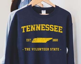 Może przedstawiać: Granatowa bluza z żółtym nadrukiem przedstawiającym stan Tennessee, z tekstem "Tennessee", "Est. 1868" i "The Volunteer State".