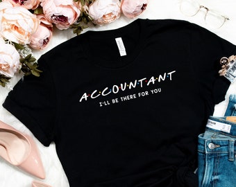 Może przedstawiać: Czarny T-shirt z białym tekstem, który brzmi "ACCOUNTANT I'LL BE THERE FOR YOU" w czcionce przypominającej popularny serial telewizyjny "Przyjaciele". Koszulka leży płasko na białym tle z parą różowych szpilek, parą niebieskich dżinsów i małą buteleczką perfum.