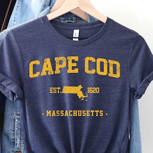 May include: A navy blue t-shirt with a yellow vintage-style graphic that reads "CAPE COD EST. 1620 MASSACHUSETTS".