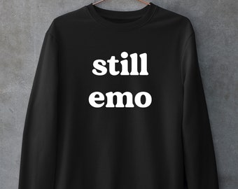 Könnte beinhalten: Schwarzer Pullover mit weißem Text, der "still emo" lautet.